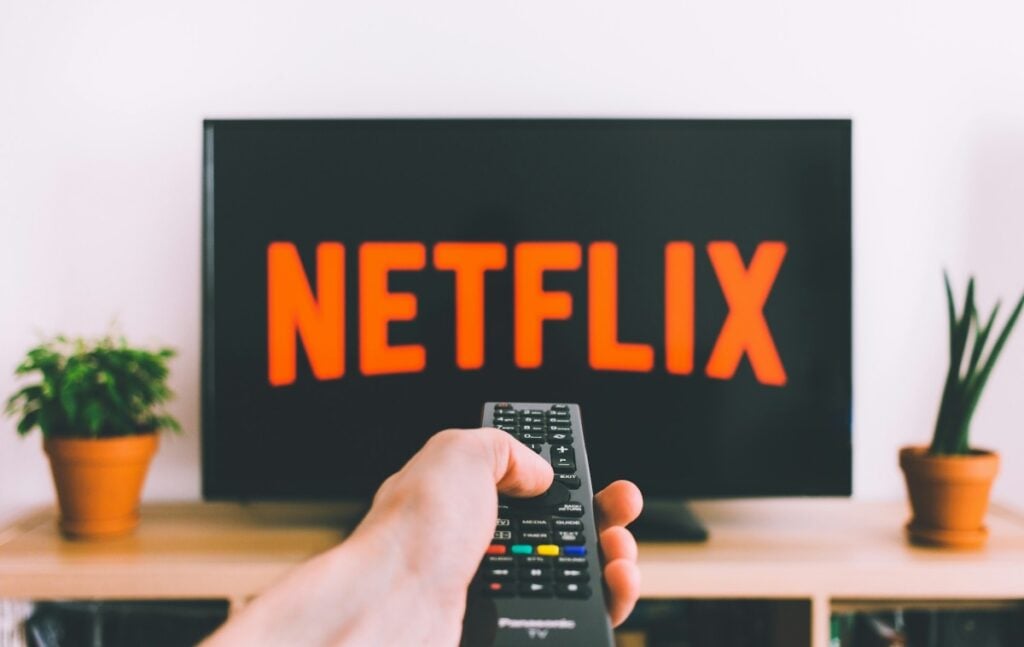 a-person-holding-a-remote-control-pointed-at-a-TV-displaying-the-Netflix-logo - Online Tech Tips person holding a remote control pointed at a TV displaying the Netflix logo