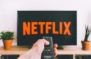 person holding a remote control pointed at a TV displaying the Netflix logo - a-person-holding-a-remote-control-pointed-at-a-TV-displaying-the-Netflix-logo