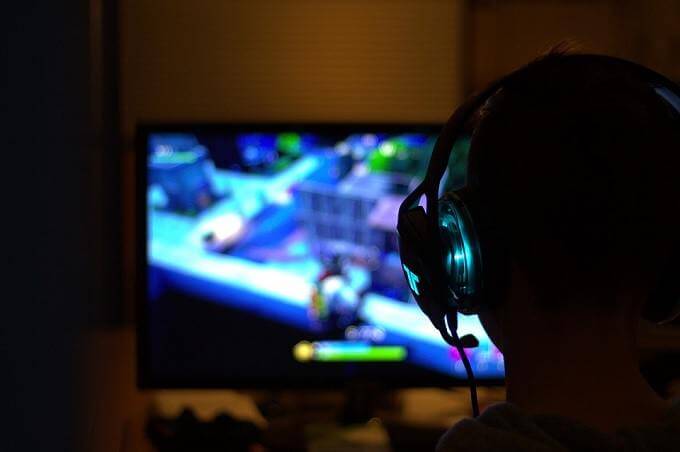 A person wearing headphones plays a video game on a computer monitor in a dark room
