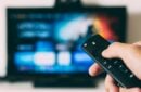 hand-holding-fire-tv-remote-with-a-blurred-TV-screen-in-the-background - hand-holding-fire-tv-remote-with-a-blurred-TV-screen-in-the-background