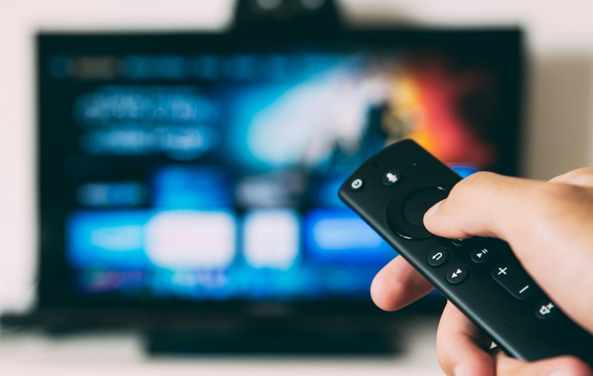 hand-holding-fire-tv-remote-with-a-blurred-TV-screen-in-the-background - Online Tech Tips A right-hand holding fire tv remote with a blurred TV screen in the background