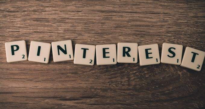 Square tiles spelling "PINTEREST" are arranged on a dark brown wooden surface