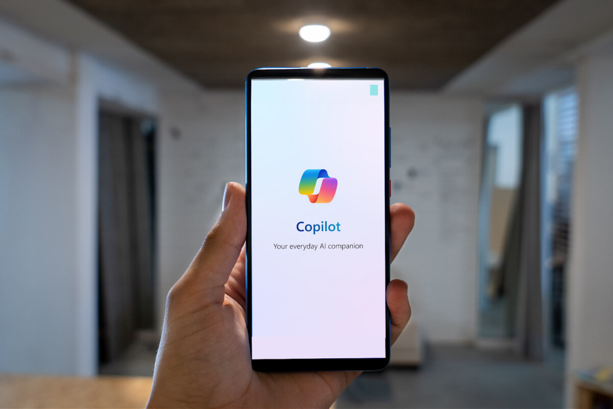 A smartphone displays the Copilot app; a hand holds it