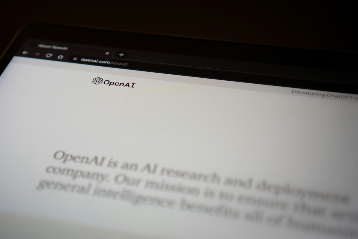 A tablet displays the OpenAI website; it shows the company logo and a description of its mission