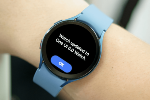 Person wearing a Samsung Galaxy Watch whose screen displays a "Watch updated to One UI 6.0 Watch." message